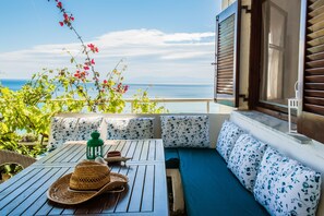 A balcony with a wooden table, a woven hat, and a green lantern. There is a sofa with floral cushions and a view of the sea. - Sunny Beachfront Home (Mola Kalyva, Halkidiki)