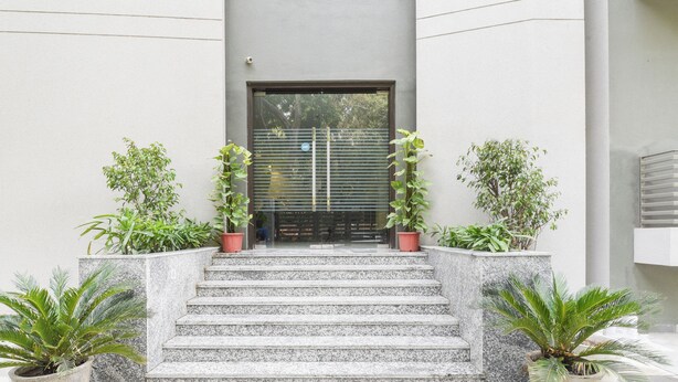 A modern building entrance with a glass door, flanked by potted plants and steps leading up to the door. - Treebo Iffco Chowk (Gurugram)