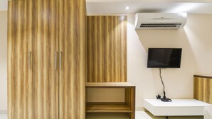 A modern room with a large wardrobe, a flat-screen TV mounted on the wall, and a small desk with a chair. - Treebo Iffco Chowk (Gurugram)