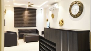 A modern reception area with a dark reception desk, a sofa, and a ceiling fan. - Treebo Iffco Chowk (Gurugram)
