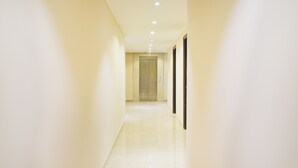 A hallway with a shiny floor, a door at the end, and a security camera on the wall. - Treebo Iffco Chowk (Gurugram)