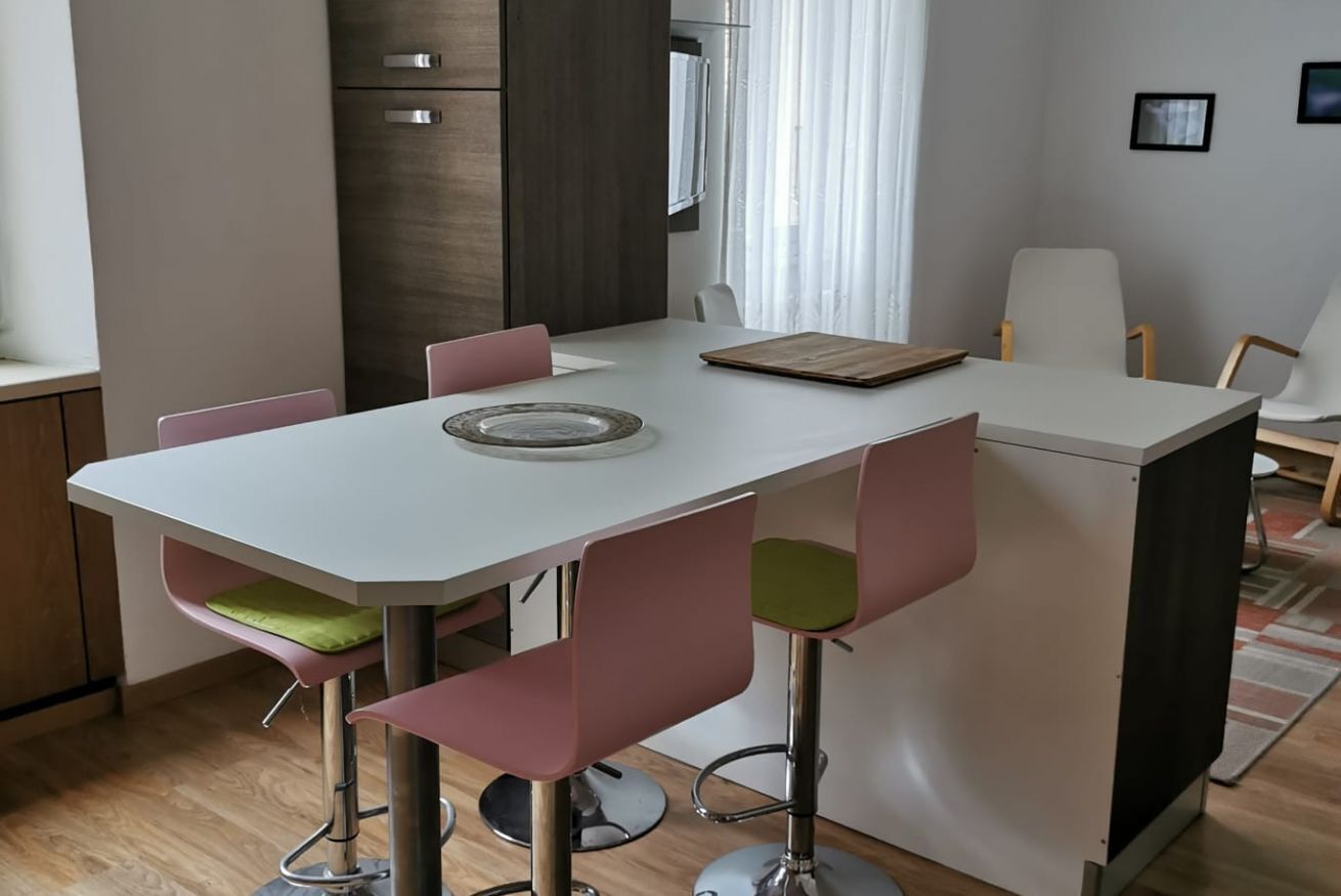 A modern kitchen with a white countertop, pink bar stools, and a wooden cutting board.