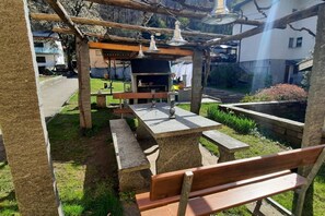 An outdoor patio with stone tables and benches, a barbecue grill, and a pergola with hanging lights.