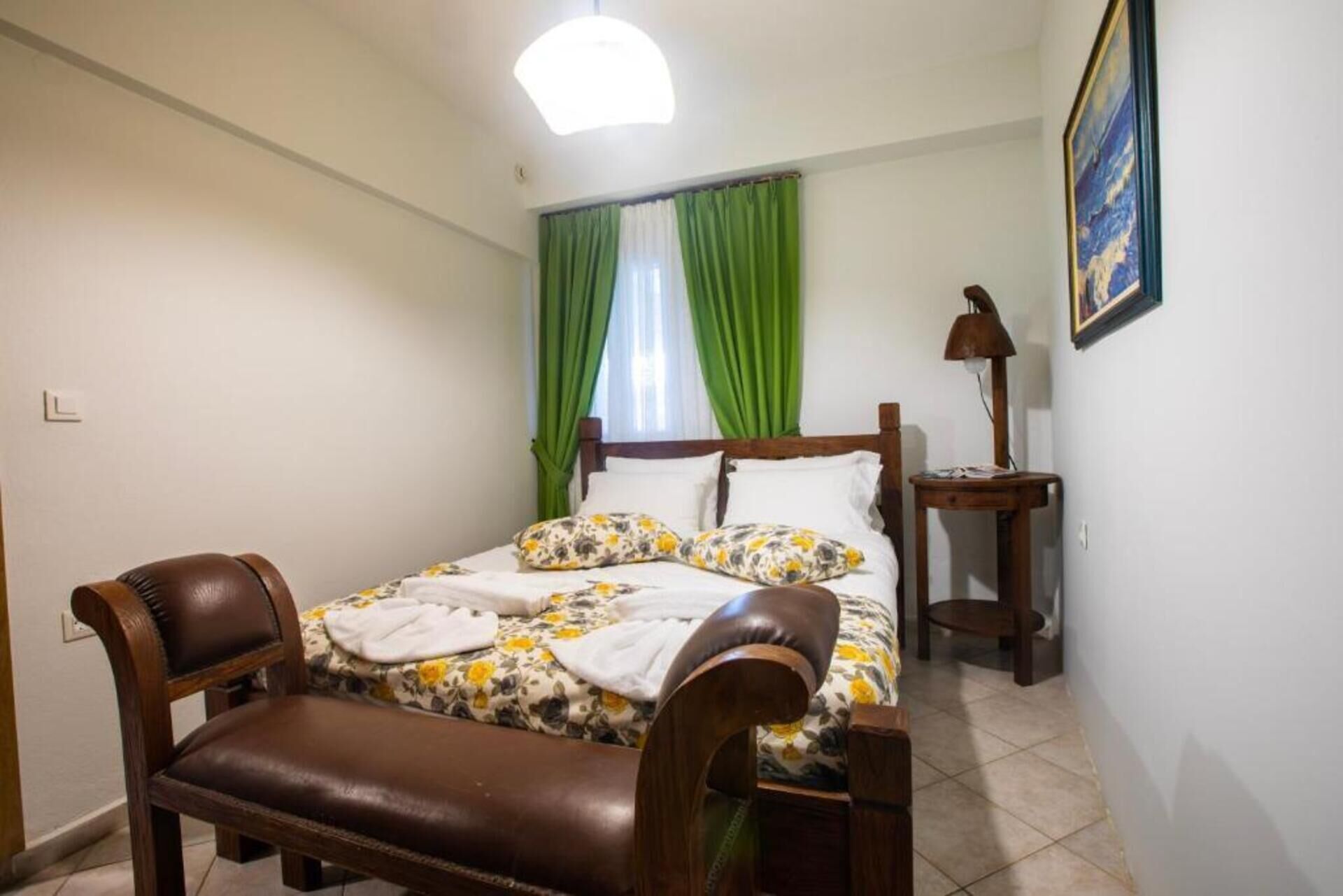 A bedroom with a bed, a bench, a lamp, and a painting on the wall.