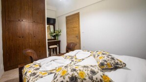 A bedroom with a bed, a wooden wardrobe, a desk with a chair, and a mirror. - Gardenia Eco Apartment in Panormo (Mylopotamos)