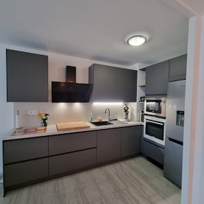 Una cocina moderna con armarios oscuros, microondas integrado y un refrigerador de acero inoxidable.