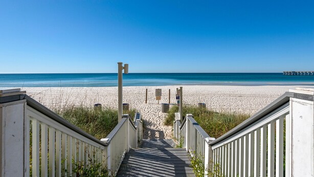 A wooden staircase leading to a beach with a clear blue sky.