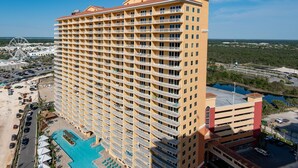 A high-rise hotel with multiple balconies, a swimming pool, and a view of a Ferris wheel in the background.