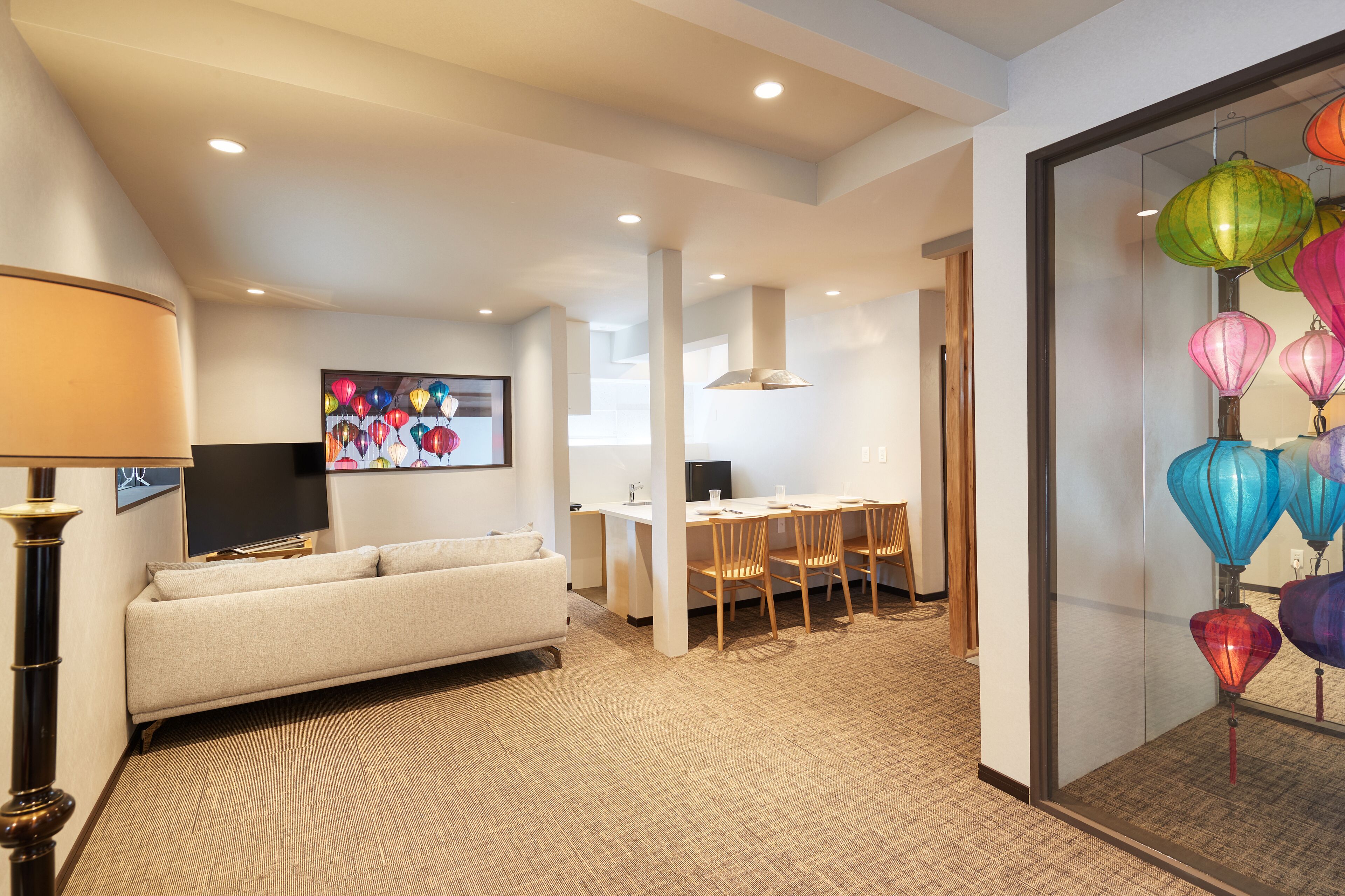 A modern hotel room with a sofa, a dining area, and colorful lanterns.