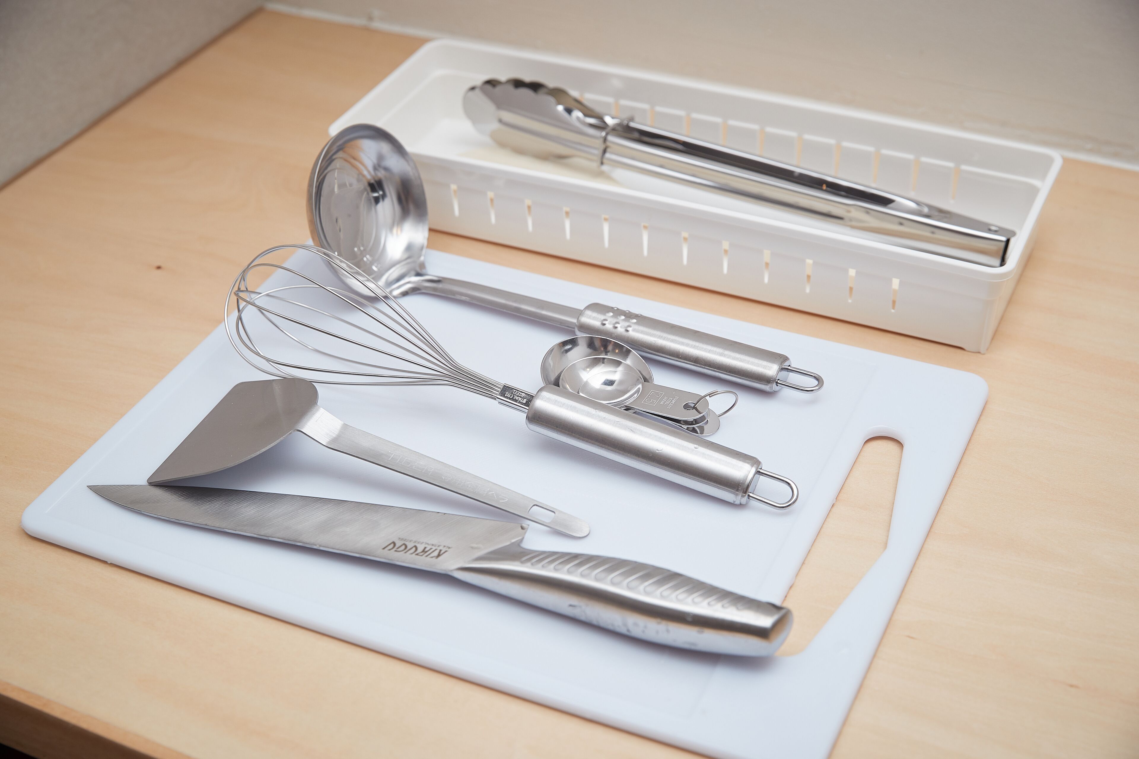 A kitchen counter with various utensils, including a whisk, a spatula, and a knife.