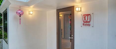 A hotel entrance with a glass door, a sign indicating 'ADAN CAMP BISEO', and a pink lantern hanging on the wall.