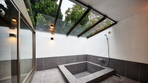 A modern bathroom with a glass-enclosed shower, a built-in bathtub, and a glass door leading to a balcony. - ADAN RESORT Lamp (Motobu)
