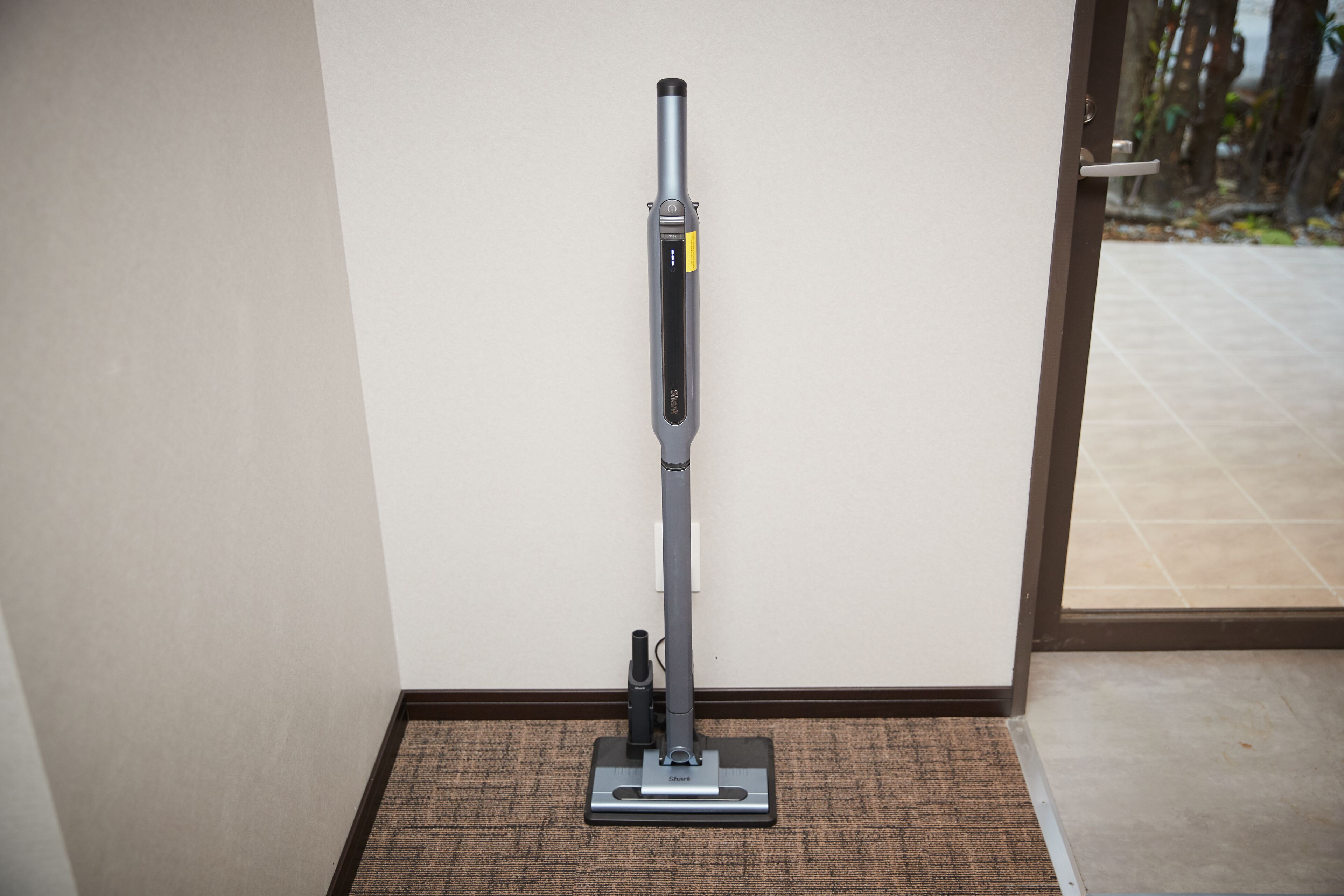 A vacuum cleaner in a corner of a room with a tiled floor and a door leading outside.