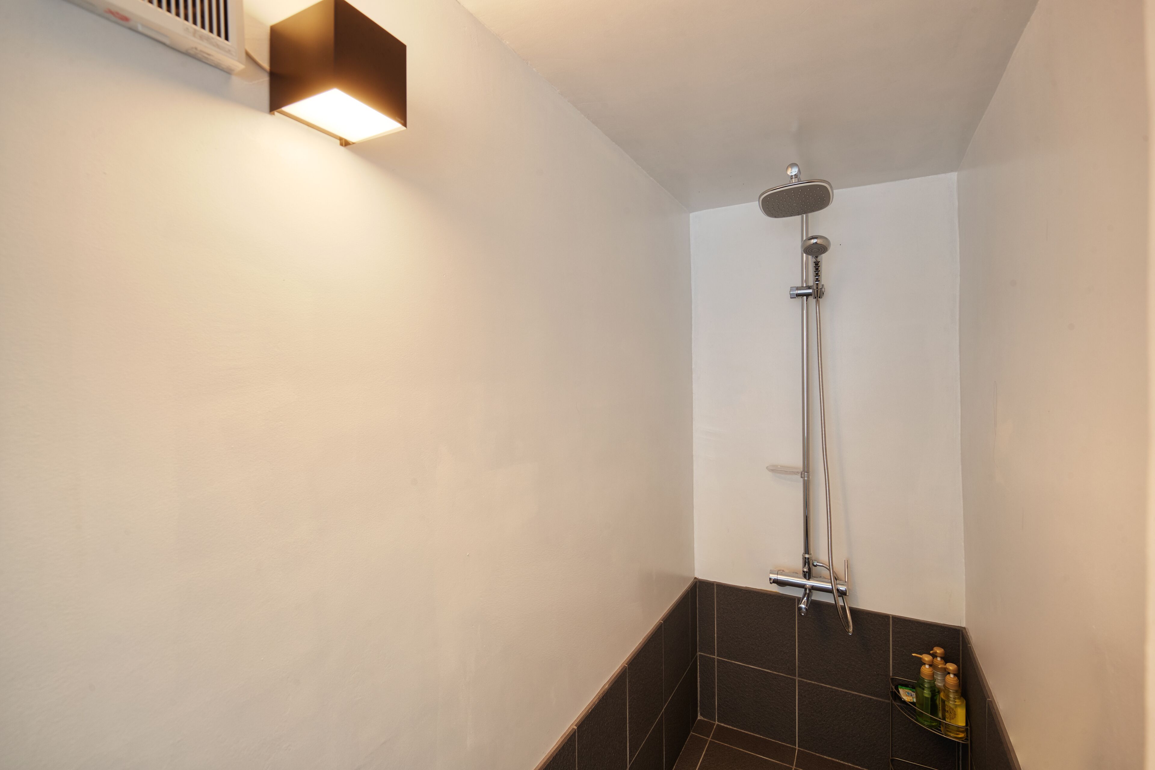 Un espacio de ducha pequeño y moderno con un cabezal de ducha manual y una lámpara de pared.
