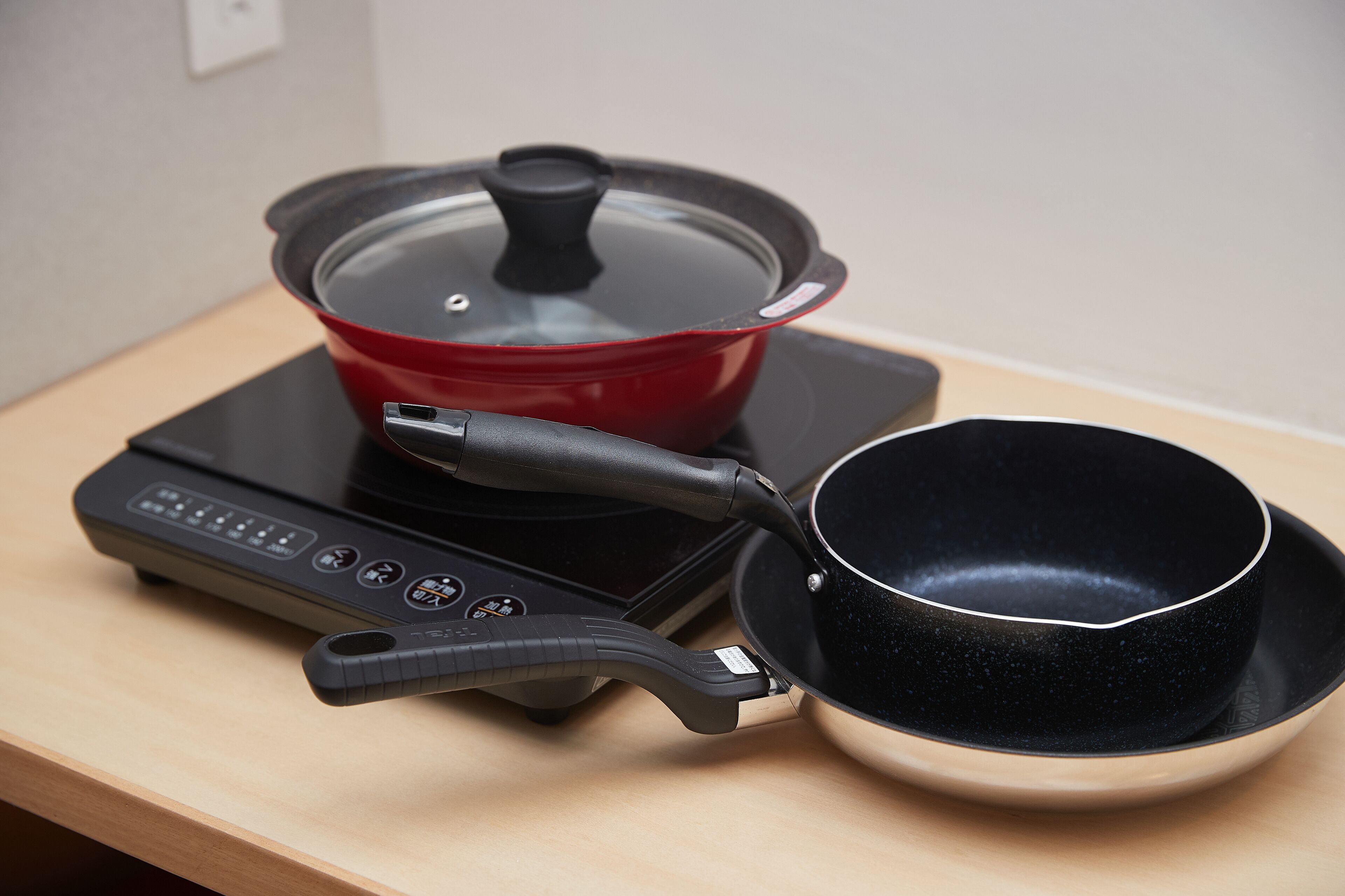 Een draagbaar inductiekooktoestel met een rode pan en een zwarte wok op een houten tafel.