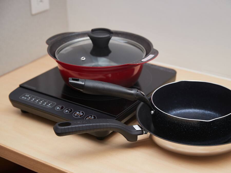 A portable induction cooktop with a red pot and a black pan on a wooden table.