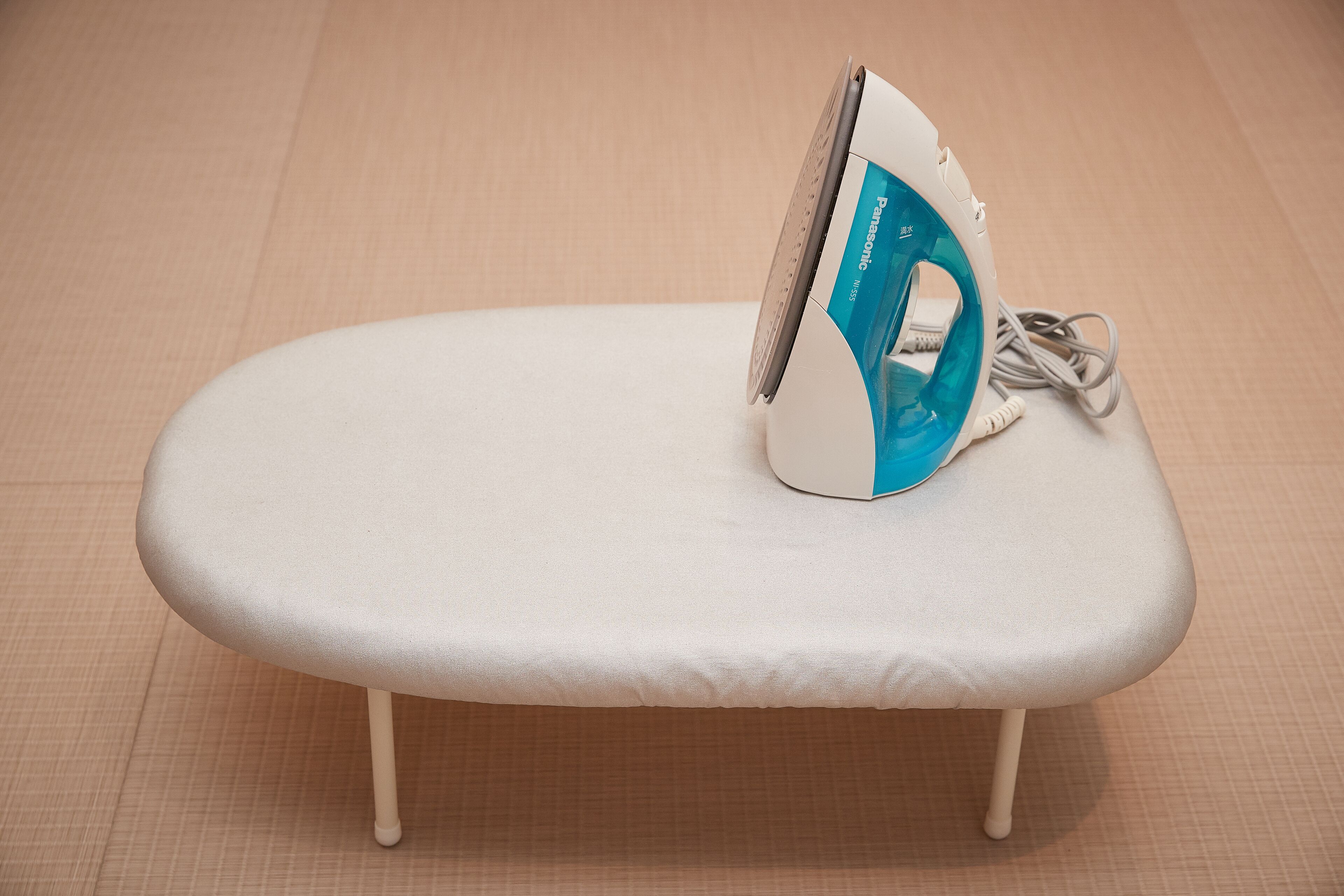 A small, white ironing board with a blue and white iron placed on it.