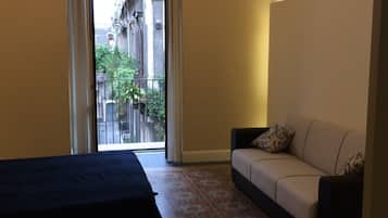 Ein Hotelzimmer mit Bett, Sofa, einem gemusterten Boden, einer Chandelierleuchtre und Blick auf Gebäude durch ein Fenster.