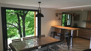 Une cuisine moderne avec un plan de travail en bois, des tabourets de bar et une grande fenêtre donnant sur la forêt.