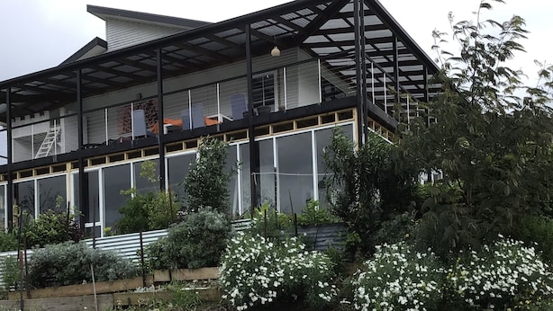 Una casa moderna con un amplio ventanal, un balcón y un jardín de flores blancas.