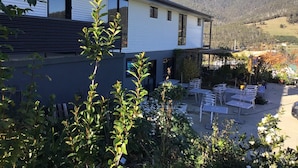 Un edificio moderno de dos pisos con un patio que tiene asientos al aire libre y vistas a un paisaje montañoso.
