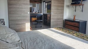 Un dormitorio moderno con una cama grande, un escritorio con silla, un televisor en la pared y una planta decorativa.