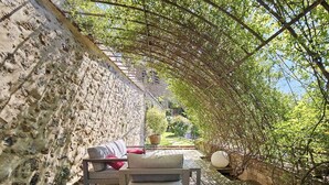 Una terraza de madera con un muro de piedra, un banco y una mesa con cojines.