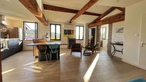 Una cocina amplia con vigas de madera, una zona de comedor con sillas y vistas a un paisaje urbano a través de amplios ventanales.