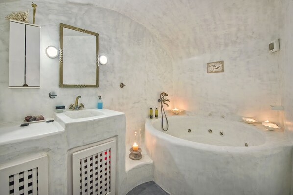 Un baño con lavamanos de mármol, bañera, espejo y un estante pequeño con objetos decorativos.