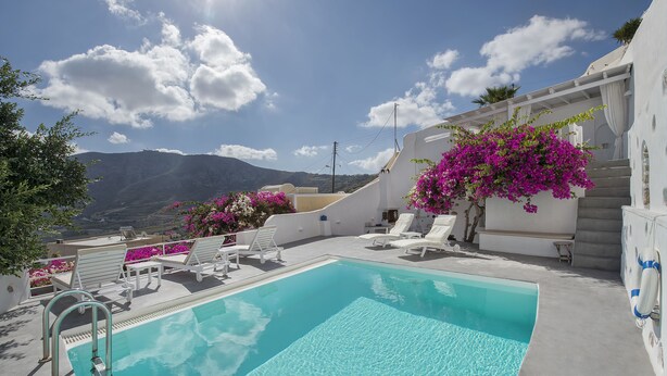 Un área de piscina con sillas de descanso blancas y una piscina azul cristalina.