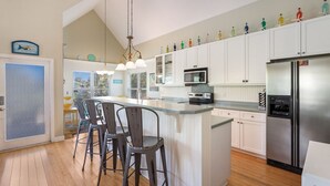 A modern kitchen with white cabinets, a stainless steel refrigerator, and a bar area with stools. - Wish Upon a Starfish by Beach Boutique Rentals (Holmes Beach)