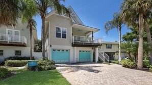 A two-story house with a covered front porch, a garage with a turquoise door, and a small balcony on the second floor. - Wish Upon a Starfish by Beach Boutique Rentals (Holmes Beach)