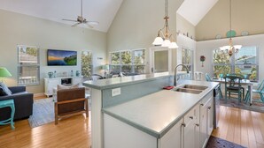 A spacious kitchen with a central island, large windows with blinds, and a ceiling fan. - Wish Upon a Starfish by Beach Boutique Rentals (Holmes Beach)