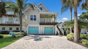 A two-story house with a covered front porch, a balcony, and a garage with a turquoise door. - Wish Upon a Starfish by Beach Boutique Rentals (Holmes Beach)
