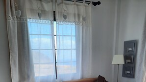 Ein Wohnzimmer mit braunem Sofa, zwei Kissen, einem weißen Tisch mit geliler Blumenarragem und einem Fenster mit transparenten Vorhängen.