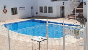 Ein Schwimmbecken mit einem umzäunten Bereich, einem Rettungsring und einer Treppe zu einer erhöhten Ebene.