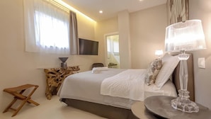 Ett modernt hotellrum med en stor säng, en platt-TV som är monterad på väggen, ett litet träbord, ett runt bord och en stor golvlampa.