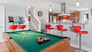 Een pooltafel met rode stoelen, een keuken met houten kastjes en een trap.