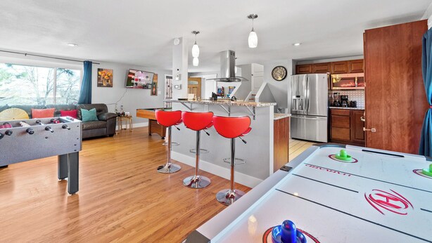 Een moderne woonkamer met een tafelvoetbaltafel, een keuken met houten kastjes en een bar met barkrukken.