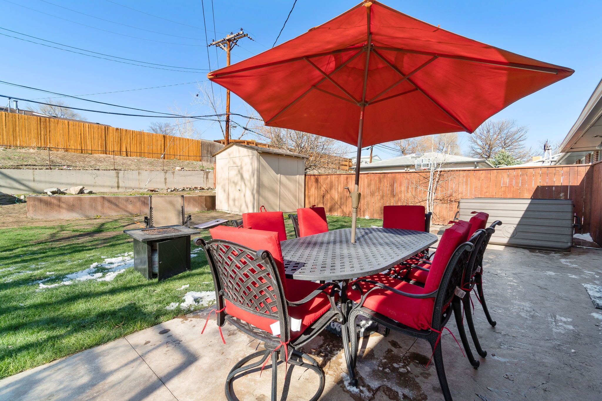 A patio with a red umbrella, metal table, and red chairs.