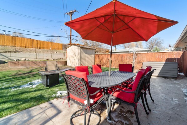 Une terrasse avec un parasol rouge, une table en métal et des chaises rouges.