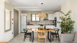 A modern kitchen with a wooden table and chairs, a hanging light fixture, and a potted plant.