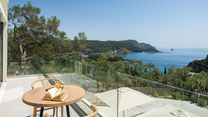 A balcony with a table, chairs, and a glass railing overlooking a coastal landscape.