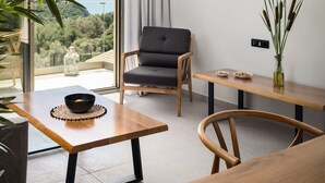 A modern living room with a view of the sea, a black chair, a wooden table, and a vase with plants.