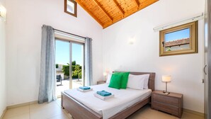 A bedroom with a large bed, a nightstand, a window with a view, and a ceiling with wooden beams.