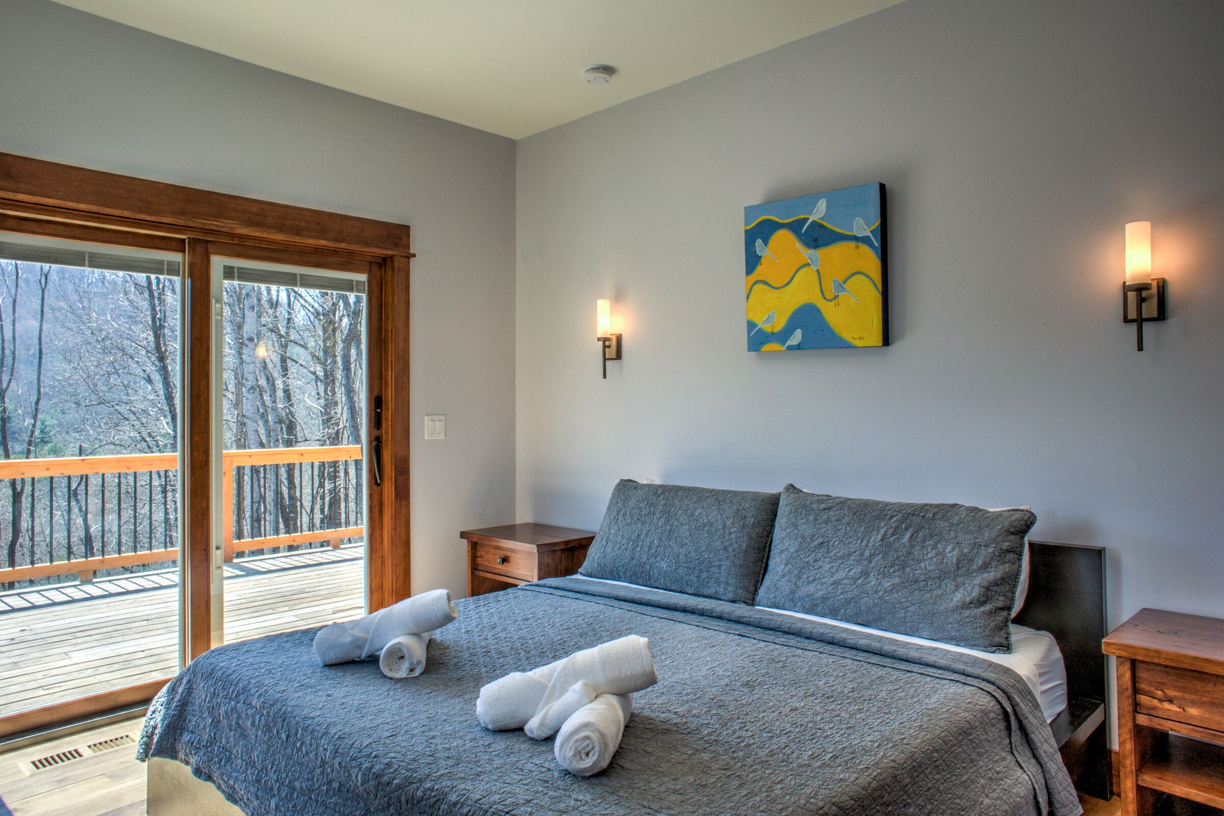 Une chambre à coucher avec un grand lit, un tableau accroché au mur et une vue sur les arbres par la fenêtre.