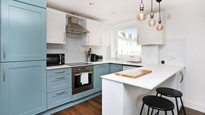 Een moderne keuken met lichtblauwe kastjes, een wit aanrechtblad, een inbouwoven en een raam dat voor natuurlijk licht zorgt.