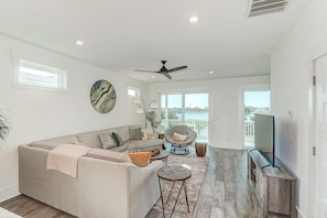 A modern living room with a sectional sofa, a round chair, a TV on a wooden stand, and a view of the outdoors.