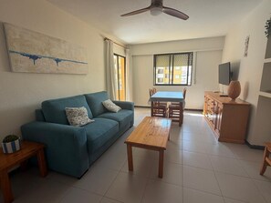 A living room with a sofa, coffee table, TV, and a dining area with chairs and a table.