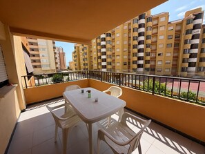 Ein Balkon mit Tisch und Stühlen, einem Geländer und Blick auf mehrstöckige Gebäude.